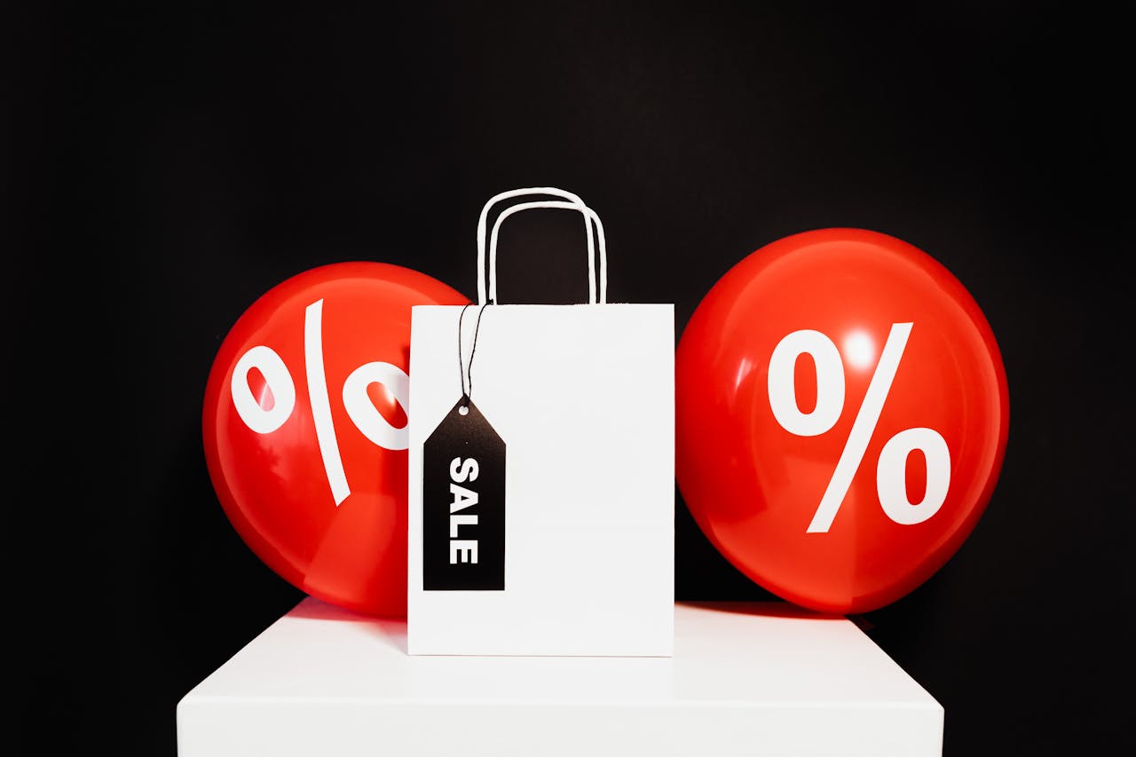 Shopping bag with sale tag and percentage balloons on black background.